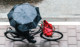 A picture containing a person riding a bicycle holding an umbrella