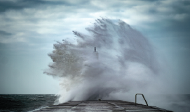 A 
picture containing a wave breaking on a jetty
